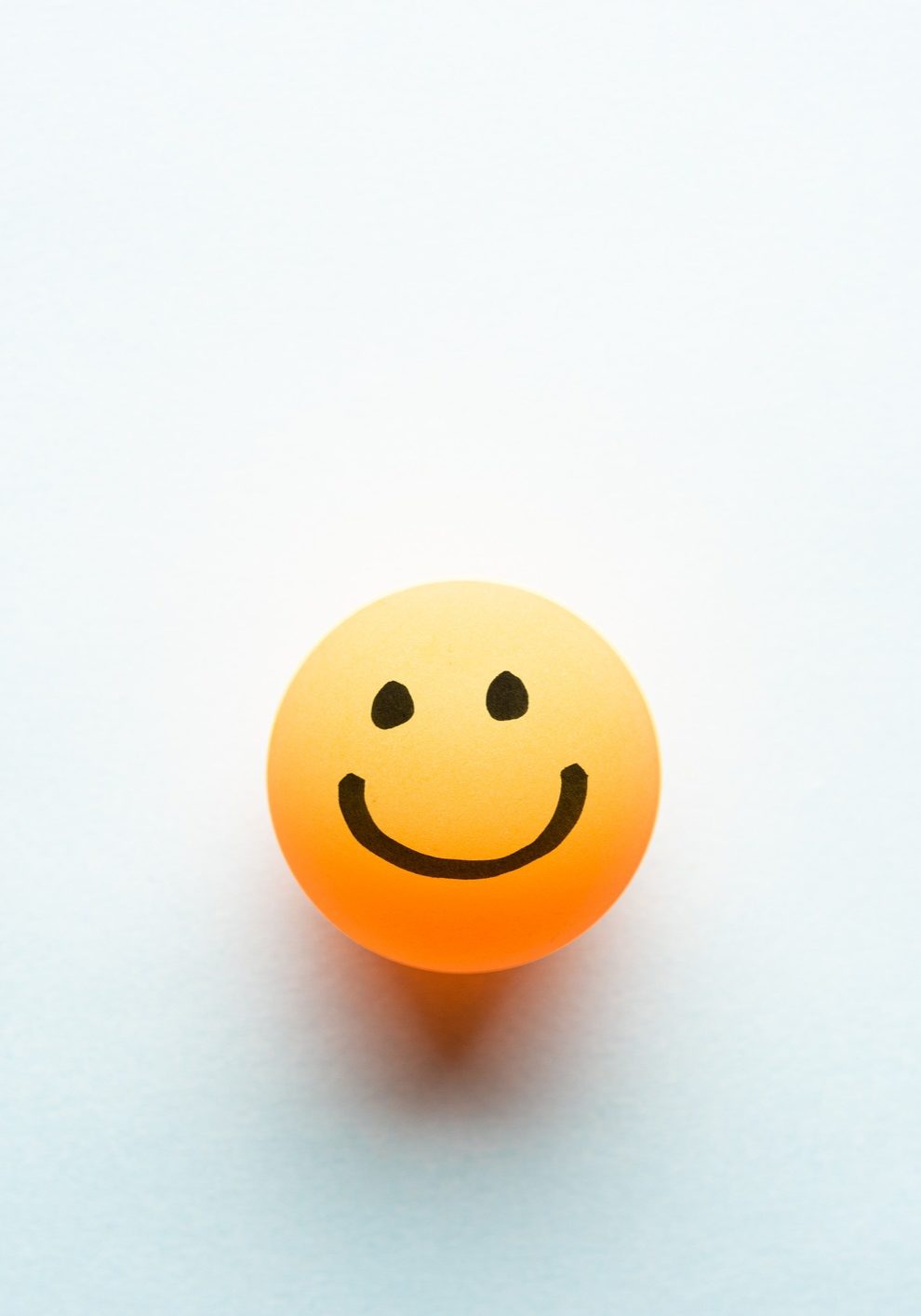 Happy smiley emoticon on a yellow ping pong ball with space for text blue background
